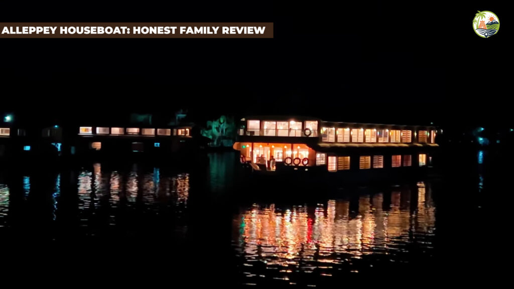 Family sitting on the deck of an Alleppey houseboat at sunset with paddy fields and coconut palms reflected on Vembanad Lake.
